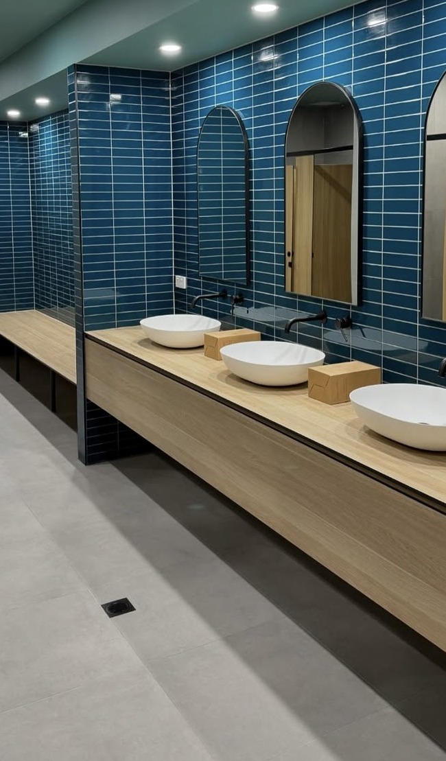Blue tiled commercial amenities with arched mirrors and a long vanity
